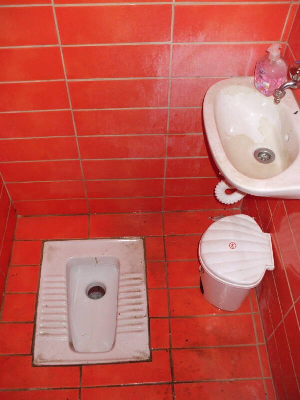 A bright orange bathroom with squat toilet at a taverna in Kastraki, Greece.