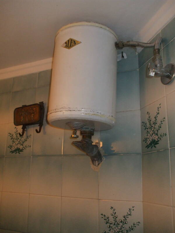Toilet flush tank mounted near the ceiling.