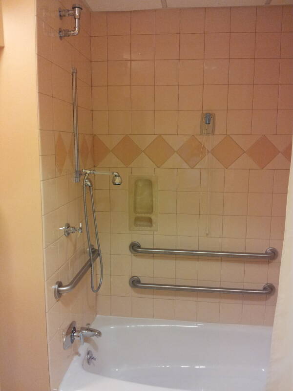 Hospital bathtub and shower with many hand rails, call cord, and adjustable shower heads.