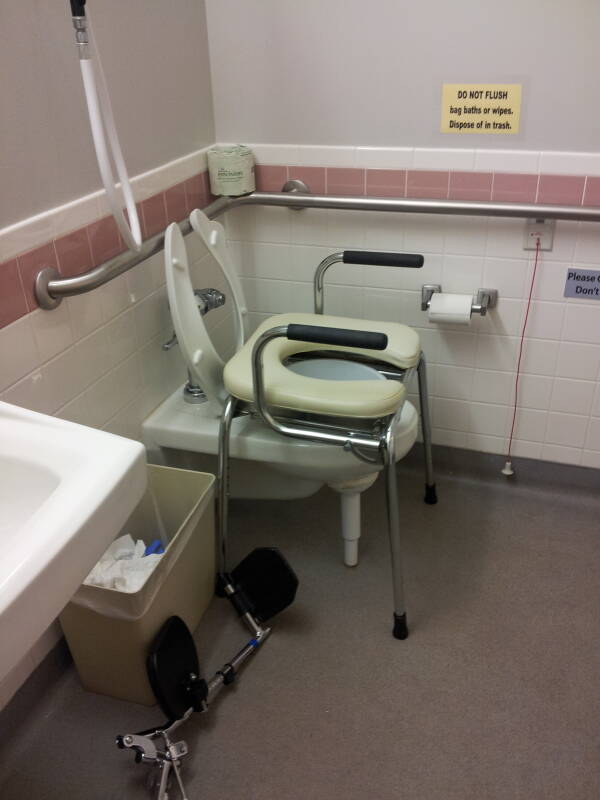 Rehabilitation facility toilet with raised seat and hand rails.