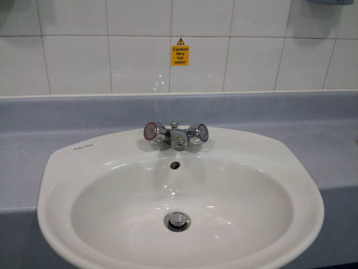 Typical British wash basin with warning label about unusually hot water.