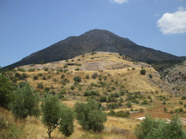 Ancient Mycenae, its hilltop in sunlight, the mountain behind is shadowed by cloud.