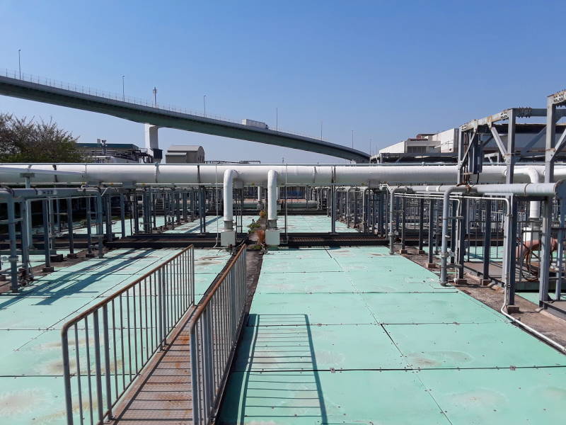 Covered sedimentation and aeration tanks and overhead pipes at the Ebie Sewage Treatment Plant in Osaka, curving overhead highway in the background.