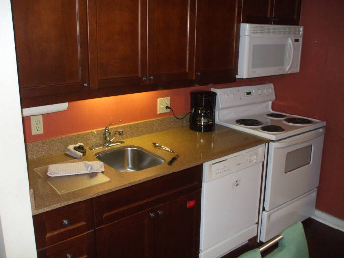 Hotel kitchen: sink, counter, cabinets, dish washer, coffee maker, kitchen stove, microwave oven.